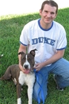 Ryan Clinton smiles while kneeling on a lawn next to a brown and white dog